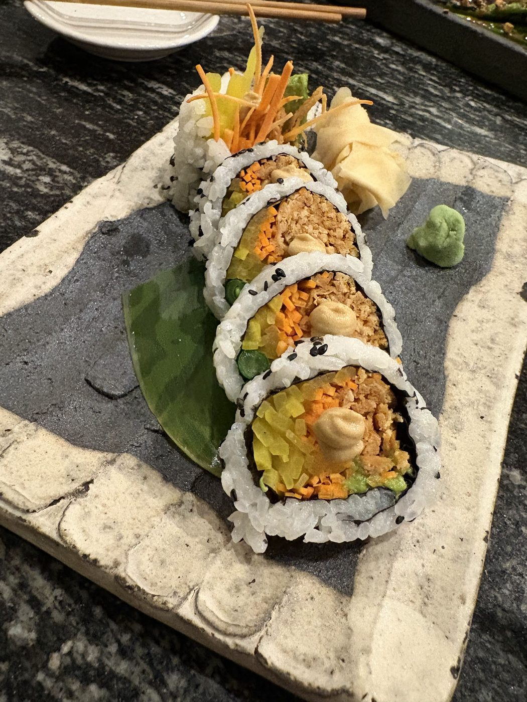 A cut sushi roll arranged on a slate board with pickled ginger and wasabi